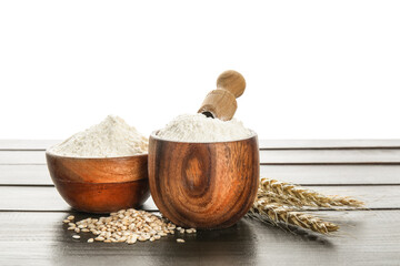 Bowls with flour, scoop and wheat ears on wooden table against white background