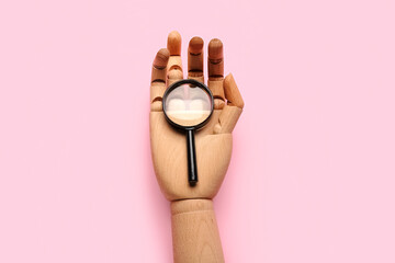 Wooden hand and magnifying glass on pink background