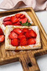 Wooden board with strawberry puff pastry on light table, closeup