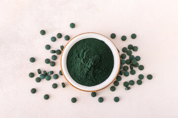 Bowl of green spirulina powder and pills on white background