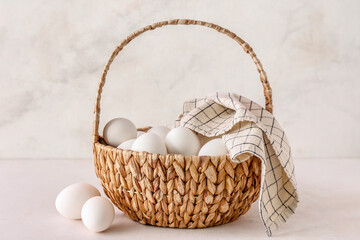 Wicker basket with white chicken eggs on light background