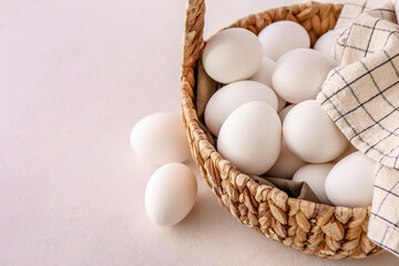 Wicker basket with white chicken eggs on light background, closeup