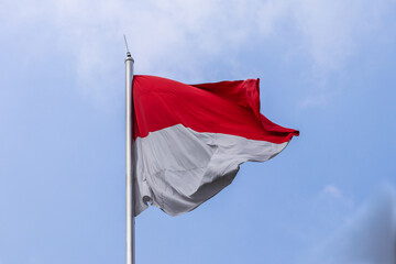 Naklejka na ściany i meble The red and white Indonesian flag fluttering in the wind isolated on a blue sky background