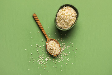 Bowl and wooden spoon with sesame seeds on green background