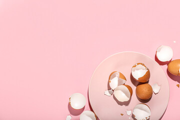 Plate with broken egg shells on pink background