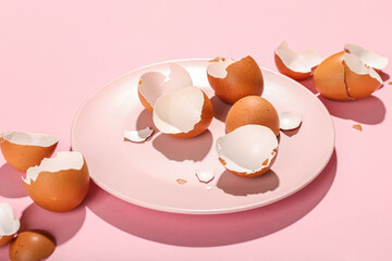 Plate with broken egg shells on pink background, closeup