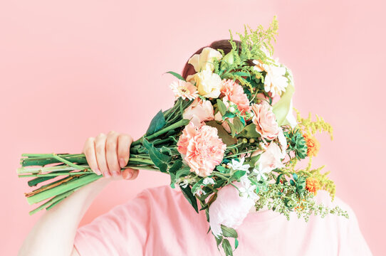 Young Woman Holding A Bouquet Of Flowers Covering Her Face On A Pink Background.