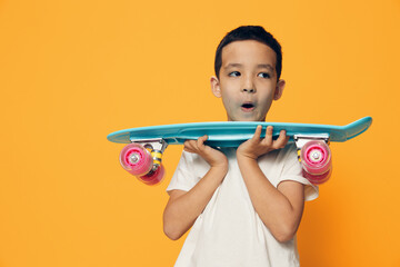 a little boy of preschool age stands on an orange background in a white T-shirt, smiling fervently holding his skate in front of him with his mouth open in surprise