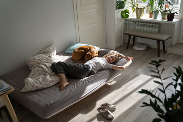 Lazy weekend. Relaxed Scandinavian 40s woman pet owner lying in bed with dog in early morning,...