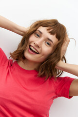 a sweet, happy, funny woman in a red T-shirt with red hair color stands on a white background and holds her head with her hands, smiling happily
