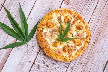 Homemade pizza with marijuana or cannabis leaves on wooden background. Fresh medical marijuana, cannabis decorate on pizza...