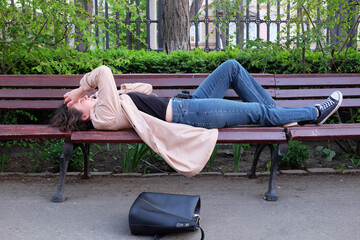a girl in a raincoat lies on a park bench and speaks on the phone