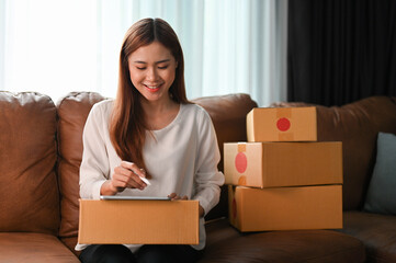 Female online shop owner packing a customer package, using a digital tablet.