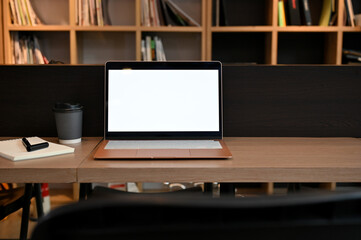 Laptop white screen mockup on a wood table in coffee shop co-working space or library.
