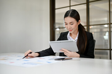 Attractive Asian businesswoman or financial worker using tablet and working with financial report