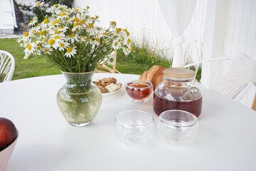 Breakfast in nature. Tea, cups, biscuits and croissants, chamomile flowers in a vase and a white gazebo in the backyard of a country house. Summer weekend morning. High quality photo