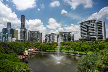 Urban park with fountain and traditional pavilion surrounded by modern skyscrapers under blue sky