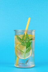 A large glass with lemon, mint and cucumber and a cocktail tube on a blue background.