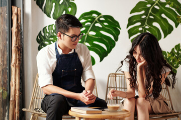Coffeeshop barista taking to his girlfriend mixing sugar in cup of coffee