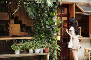 Young woman opening door of modern cozy coffeeshop with walls decorated with lush plants