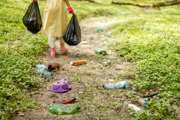 Fototapeta premium Scattered plastic garbage on dried river in the woods and woman going with bags on background. Problem of ecology and environmental pollution