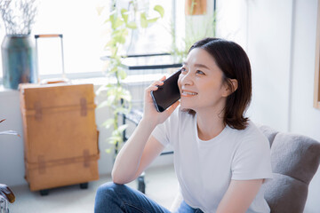 明るい室内でスマートフォンで笑顔で通話する日本人女性