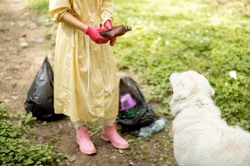 Woman in protective clothes twists a plastic bottle while collecting garbage in the woods, cropped...
