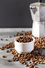 Roasted coffee beans in a white mug, coffee beans scattered around. 