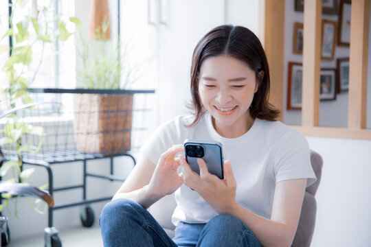 明るい室内でスマートフォンで笑顔で通話する日本人女性