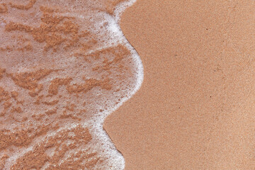 A soft wave runs on a sandy shore on a summer day. Empty space can be used as background for...