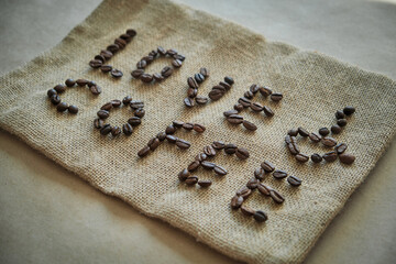 Inscription love coffee from coffee beans on burlap background. Banner for cafe or coffee shop advertising in rustic style. Roasted arabica on jute bag backdrop, close up.