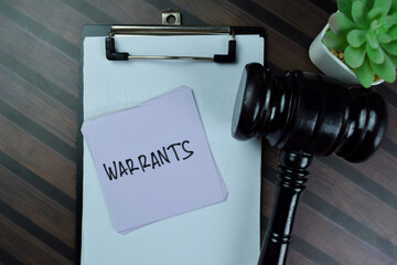 Concept of Warrants write on sticky notes with gavel isolated on Wooden Table.