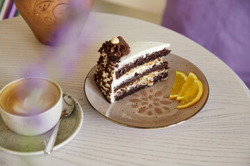 Chocolate piece of cake and cup of cappuccino on wooden table in the cafe. Aesthetic coffee time. Time for yourself. Lavander in the jug.
