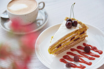Cherry, raspberry biscuit cake, cup of cappuccino on wooden table outside. Pink flowers decorations in the cafe terrace. No sugar, natural sweets.