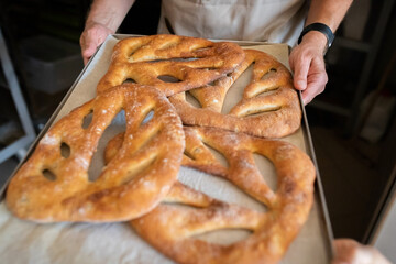 A man in a bakery takes traditional French Fougasse bread out of the oven. Front view.
