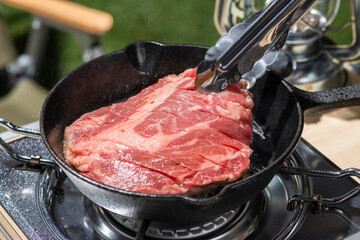 アウトドアのキャンプ場でスキレットを使ってステーキ肉を焼く