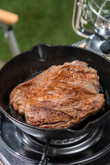 アウトドアのキャンプ場でスキレットを使ってステーキ肉を焼く