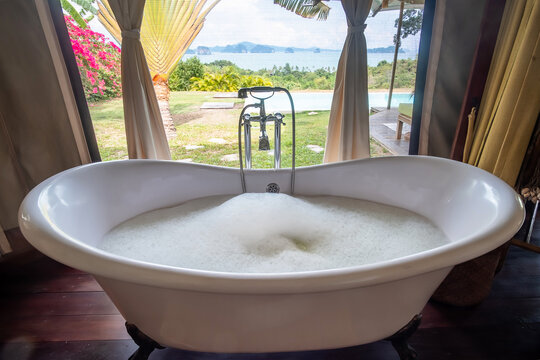 bathtub with foam bubbles in tropical luxury resort against beautiful ocean background. Spa and relaxation concepts
