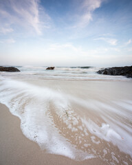 Wide sandy beach with receding waves and swirling sea foam patterns