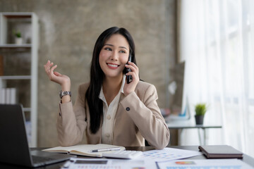 Happy young Asian business woman talking on the phone in the office.