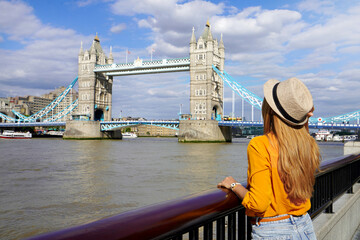 Tourist girl leaning on the railing on River Thames promenade with Tower Bridge famous landmark in London, UK