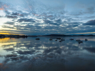 Aerial sunrise waterscape with boats, reflections and cloud filled sky