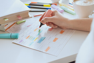Planning process for the week. The girl makes a training schedule for the week. White table with colorful markers and stickers. Selective focus. Side view.