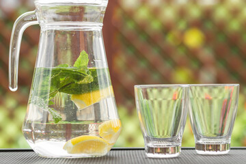 Glass jug of cold detox water with lemon slices and mint leaves. Refreshing drink in hot summer day.