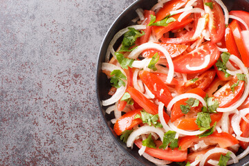Delicious homemade tomato salad with onion and cilantro seasoned with olive oil close-up in a plate on the table. Horizontal top view from above