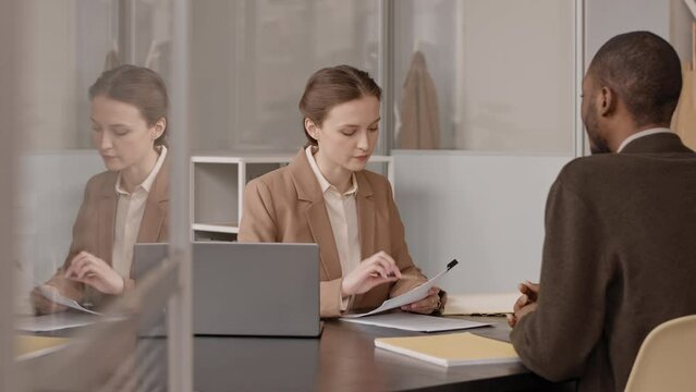 Medium slowmo of female hr manager interviewing young Black man, sitting in front of each other at office desk