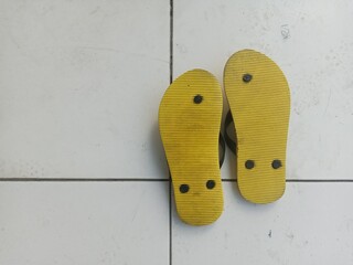 a pair of yellow flip-flops upside down on a white tiled floor
