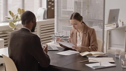 Medium slowmo of young African American man giving his resume or cover letter to female hr manager while having job interview in office