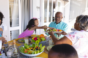 Multiracial grandparents serving fruits to granddaughter while having lunch at dining table at home
