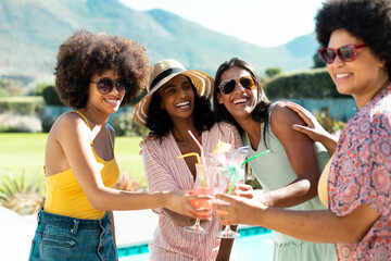 Happy biracial young female friends toasting cocktails while having fun at pool party in summer - Powered by Adobe